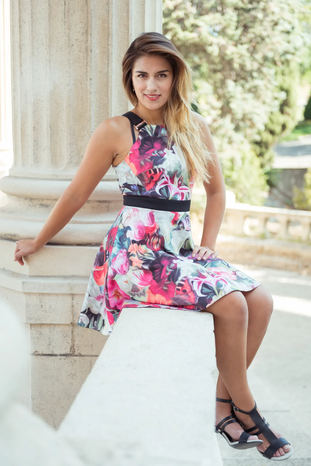 Woman in a floral dress posing beside pale stone columns.