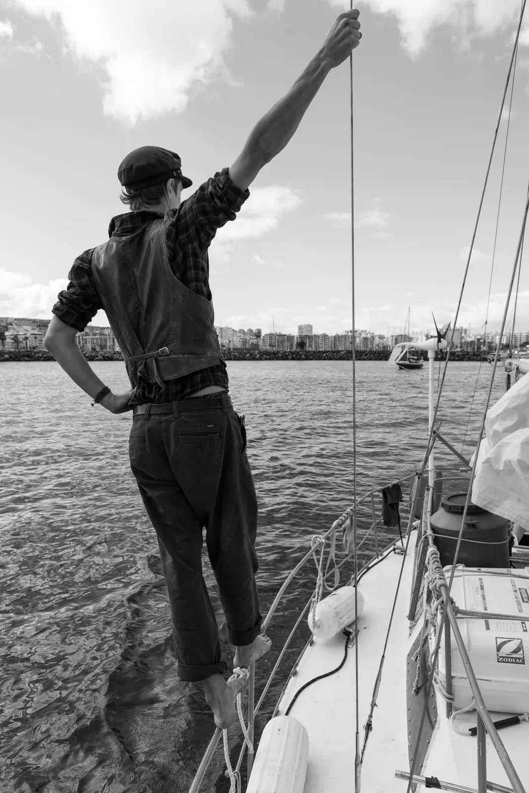 Person standing beside the rigging of a sailboat in black and white