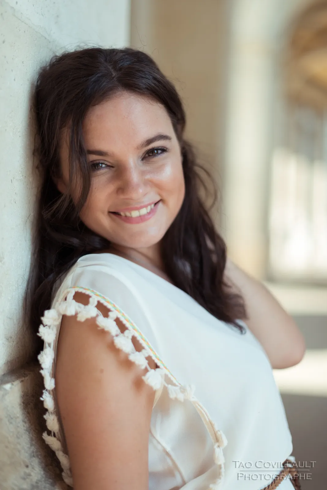 Portrait of a woman in a white dress beside a stone column.