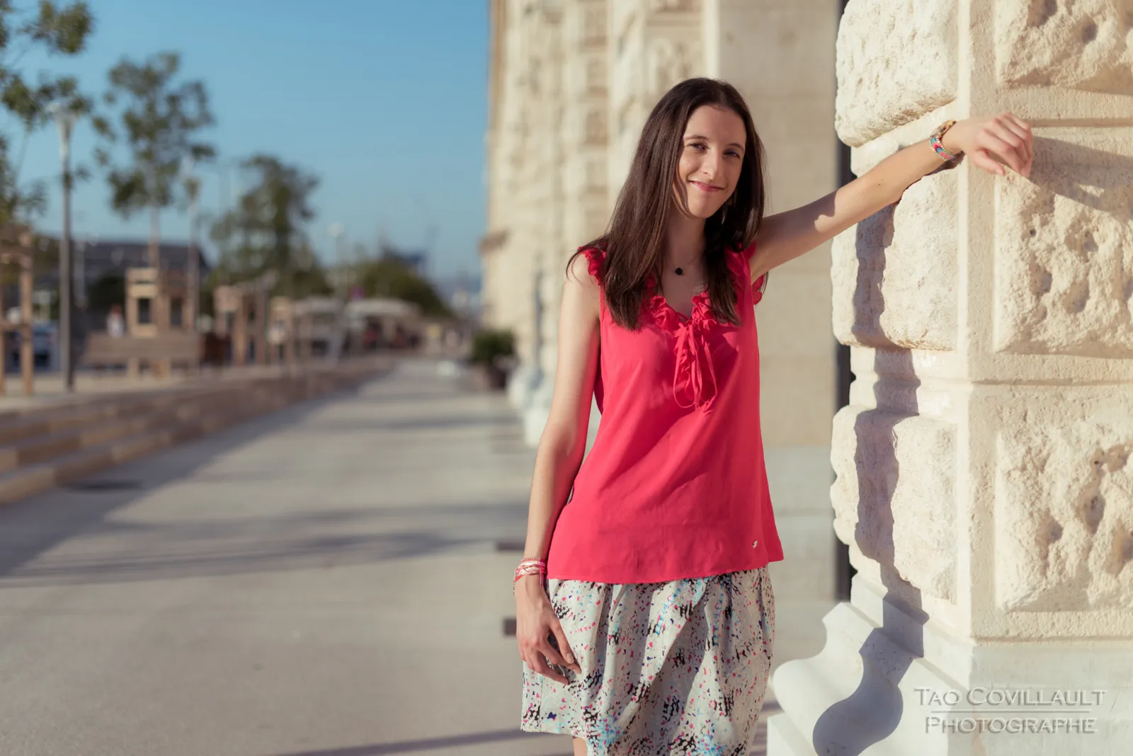Woman in a bright pink top and patterned skirt posing beside stone steps and walls.