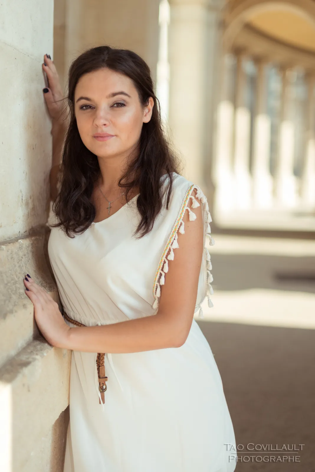 Portrait of a woman in a white dress beside a stone column.