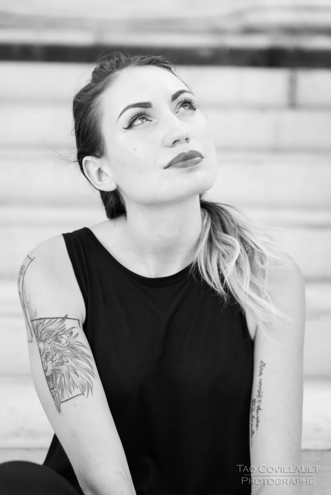 Black-and-white photograph: woman in black clothing posing on pale stone steps.