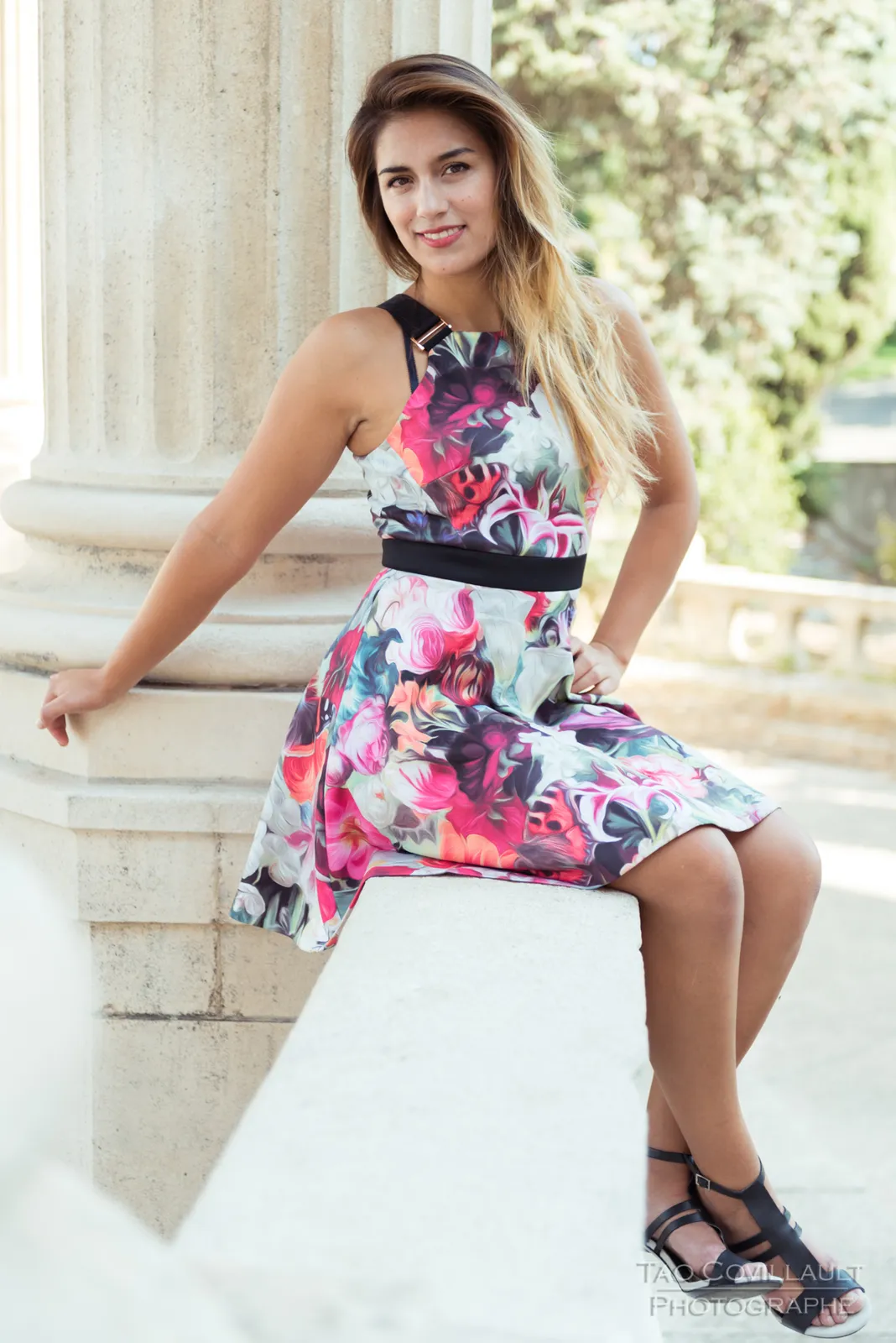 Woman in a floral dress posing beside pale stone columns.