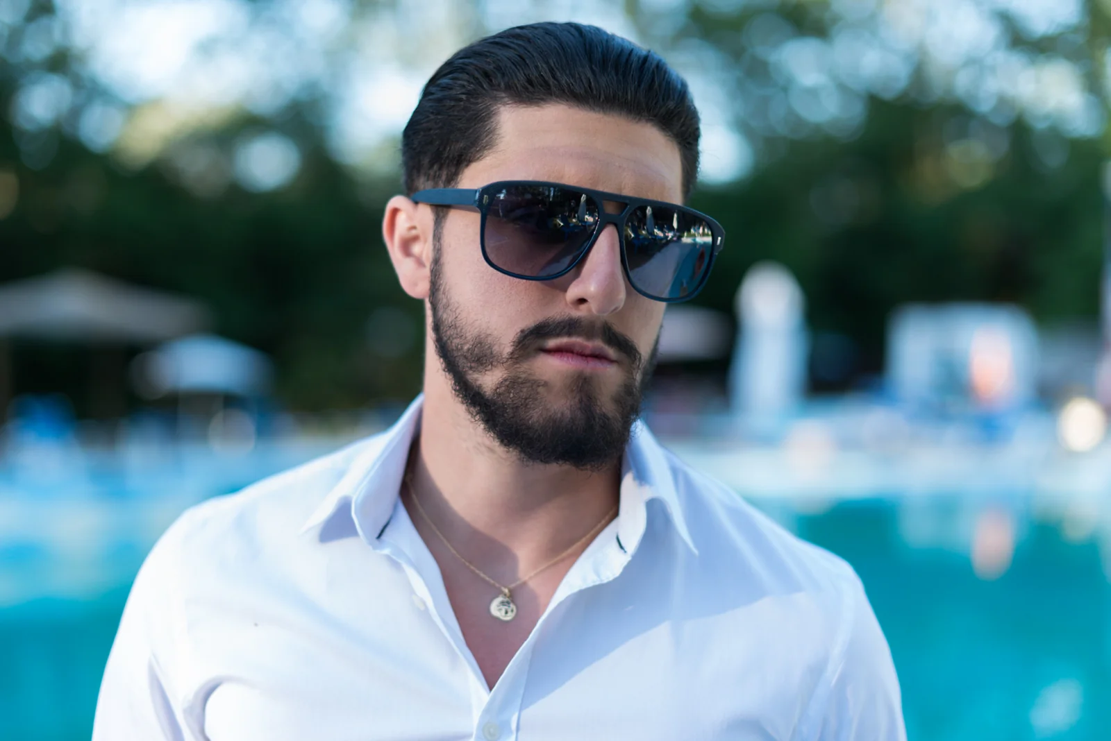 Man wearing sunglasses and a white shirt beside a swimming pool.
