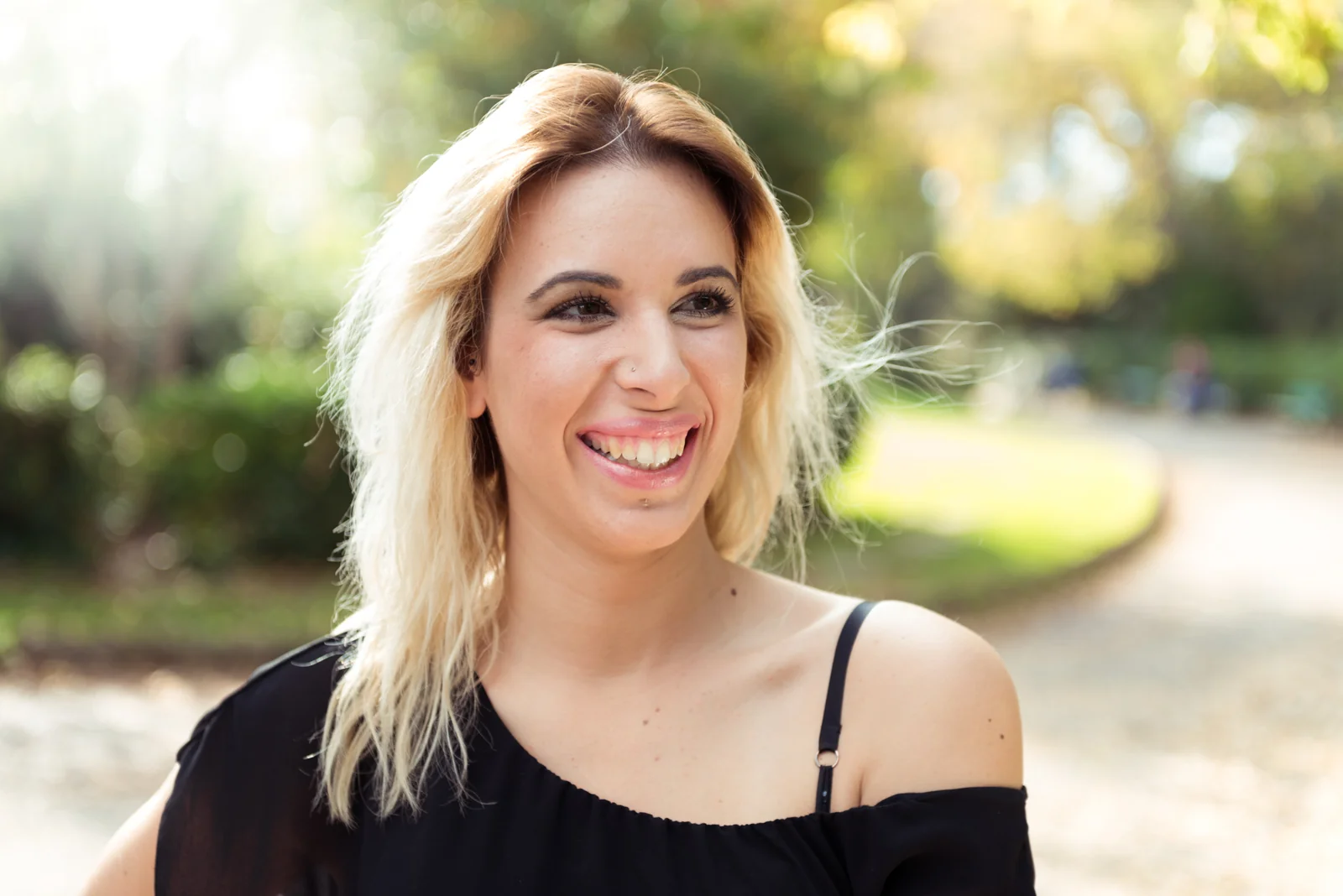 Woman in a black top and jeans posing in a leafy park.