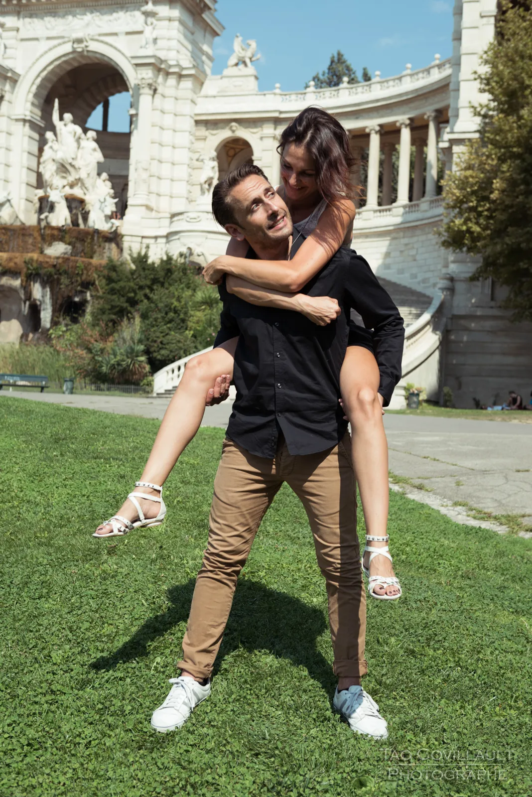 Couple posing playfully on a lawn in front of an ornate building.
