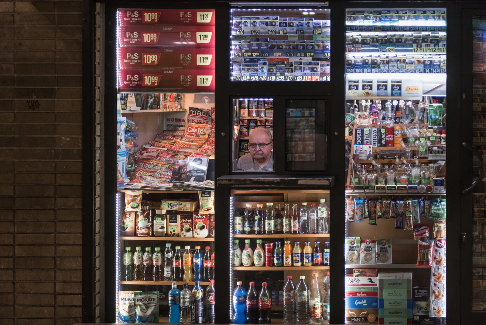Shop attendant framed by shelves of drinks and cigarettes