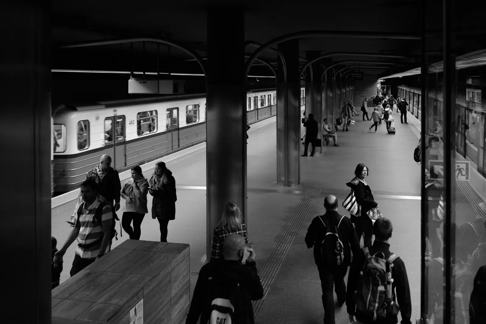 Passengers beside a train under a station roof in black and white