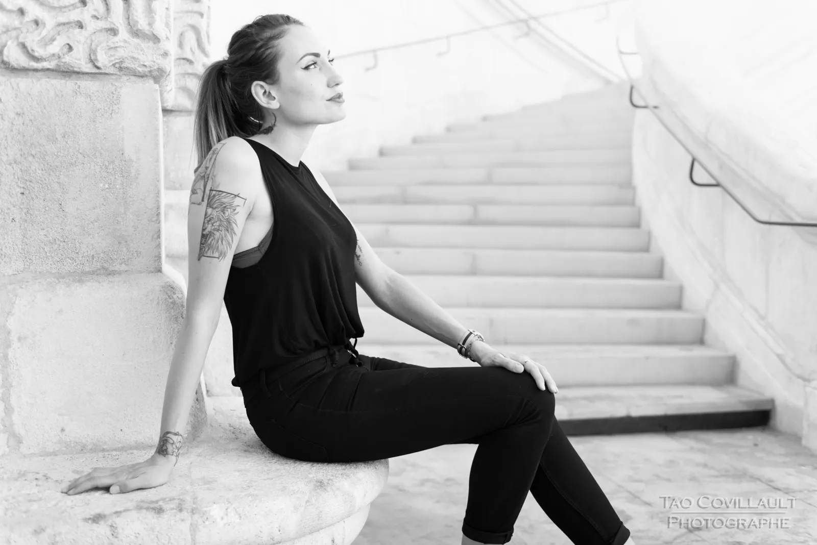 Black-and-white photograph: woman in black clothing posing on pale stone steps.