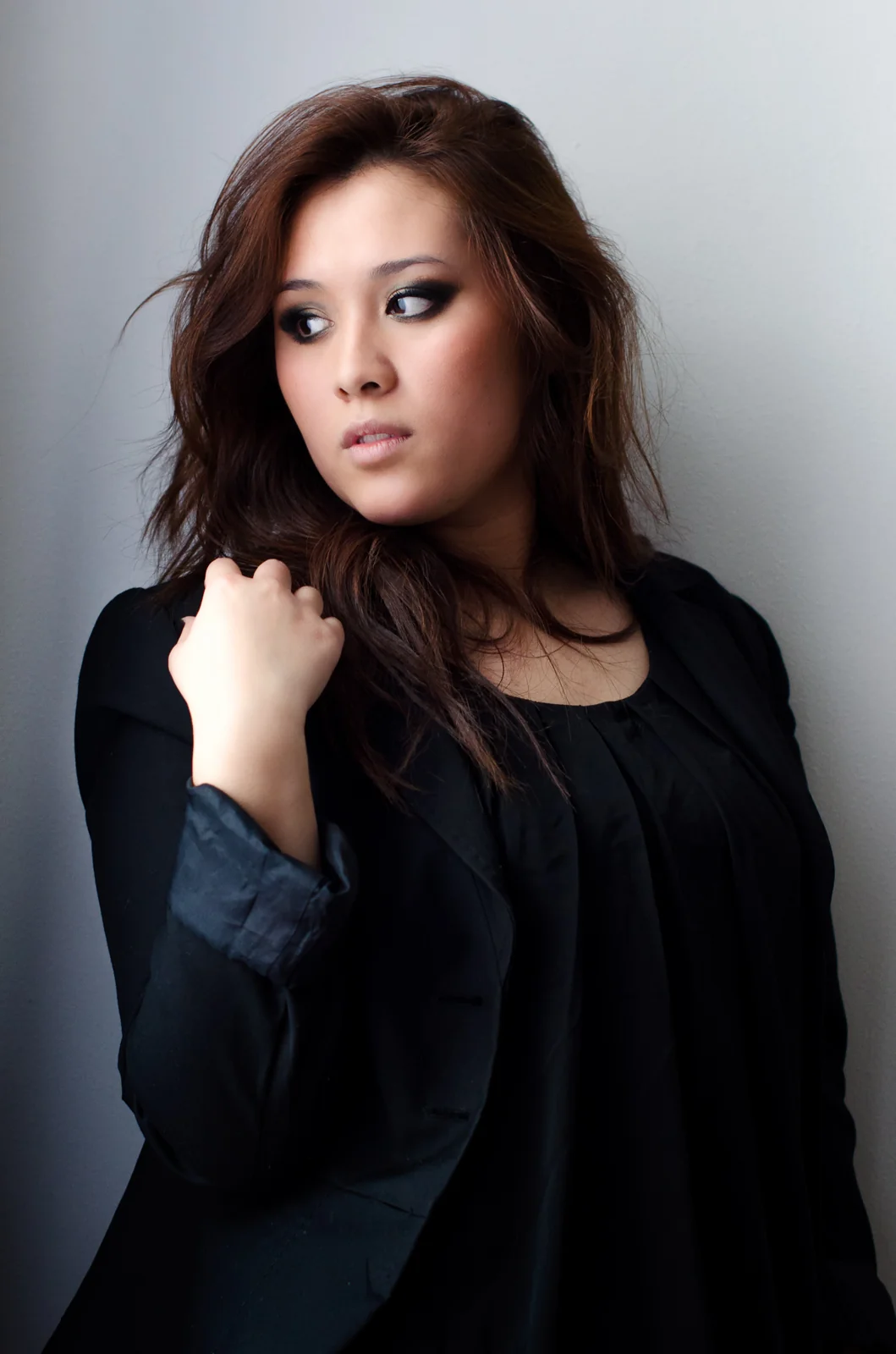 Woman in a black top touching her hair against a pale wall.
