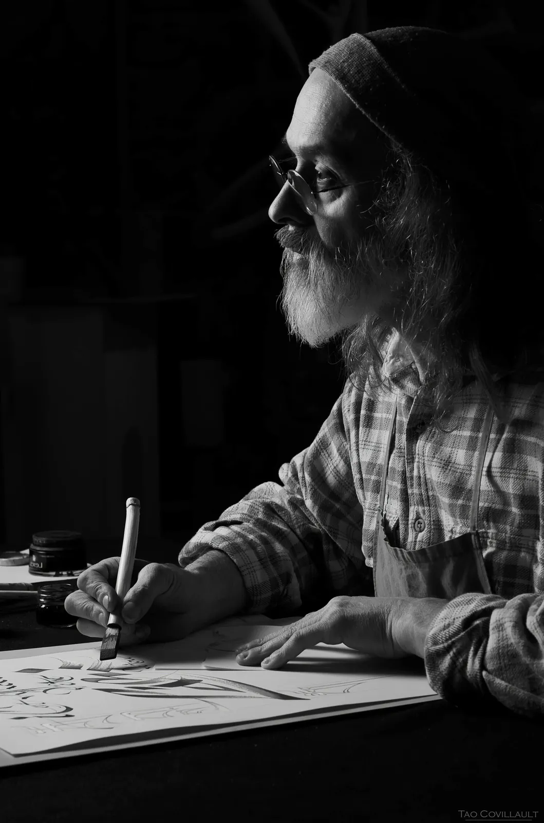 Bearded person writing at a table in black and white