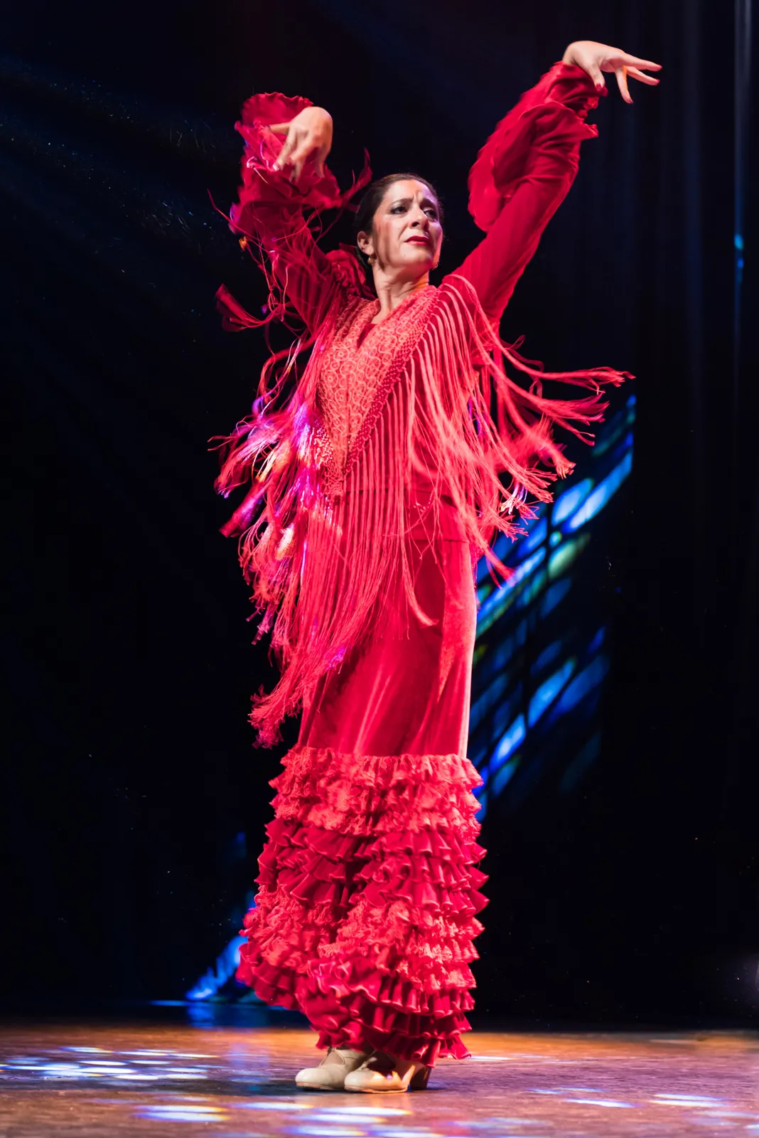 Flamenco dancer lifting her arms in a red fringed dress.