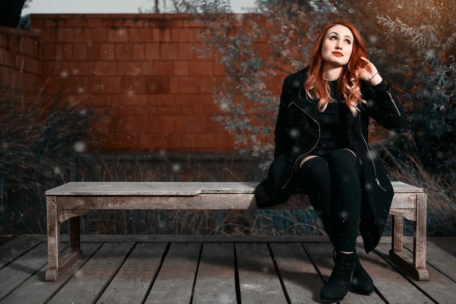 Woman dressed in black seated on a bench against a brick wall.