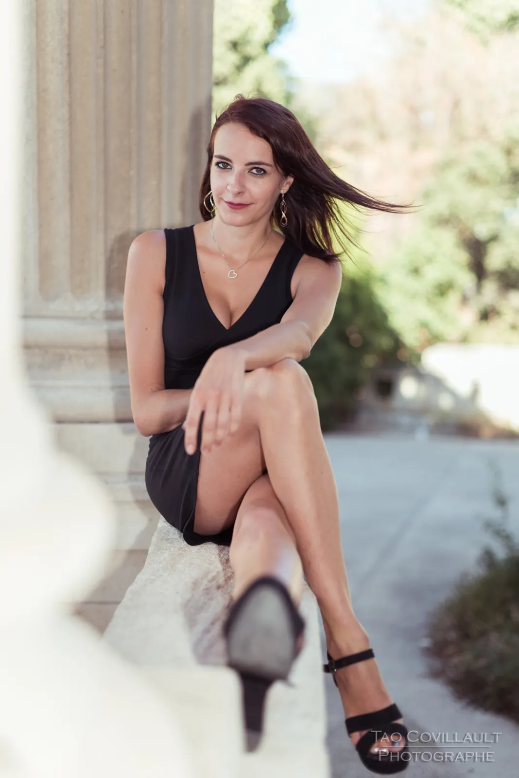 Woman in a black dress posing near pale stone columns.