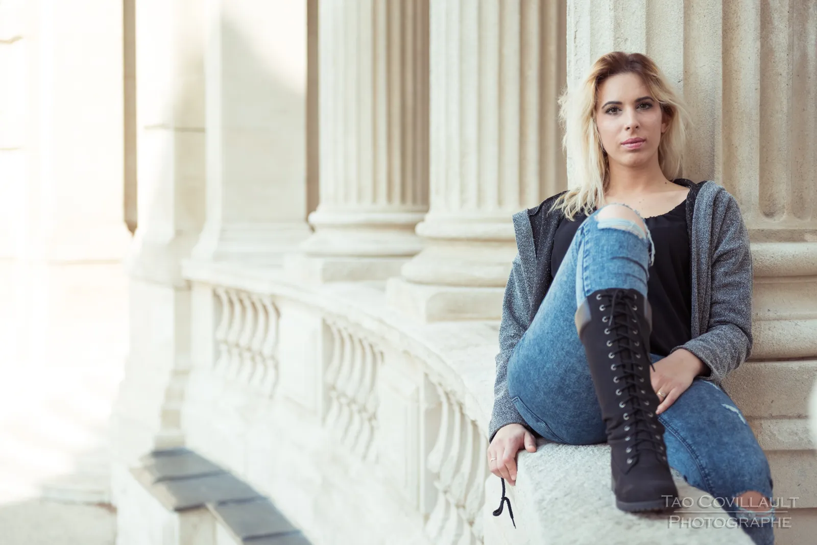 Woman in jeans and a dark jacket posing beside stone columns.