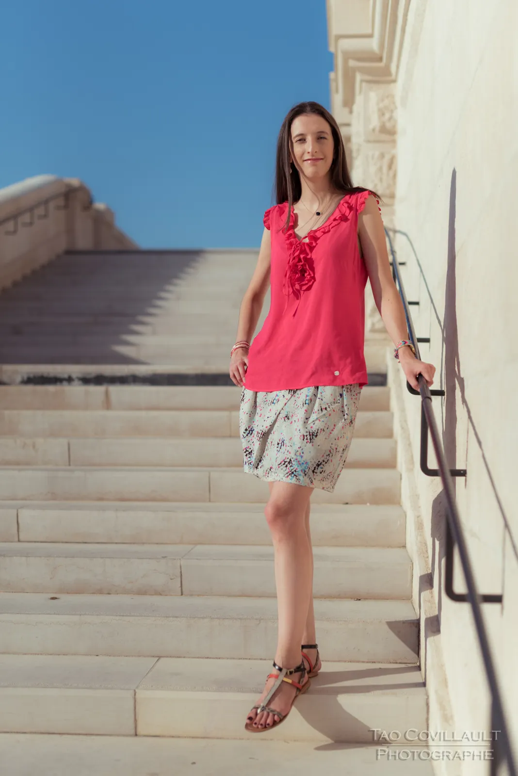 Woman in a bright pink top posing beside broad stone steps.