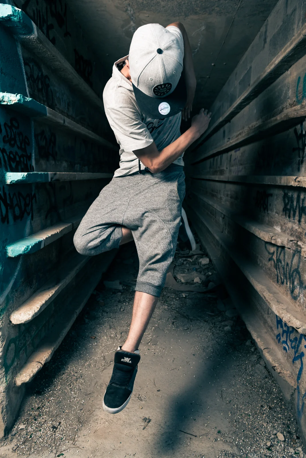Dancer in a cap posing between industrial walls.