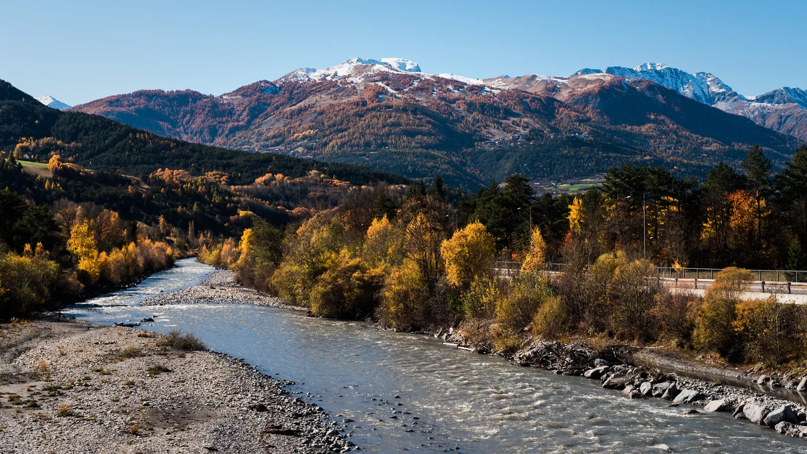 River winding through autumn trees beneath snowy mountains
