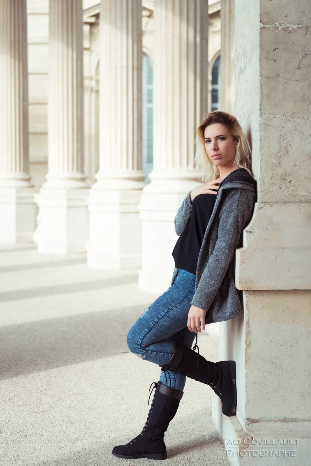 Woman in jeans and a dark jacket posing beside stone columns.