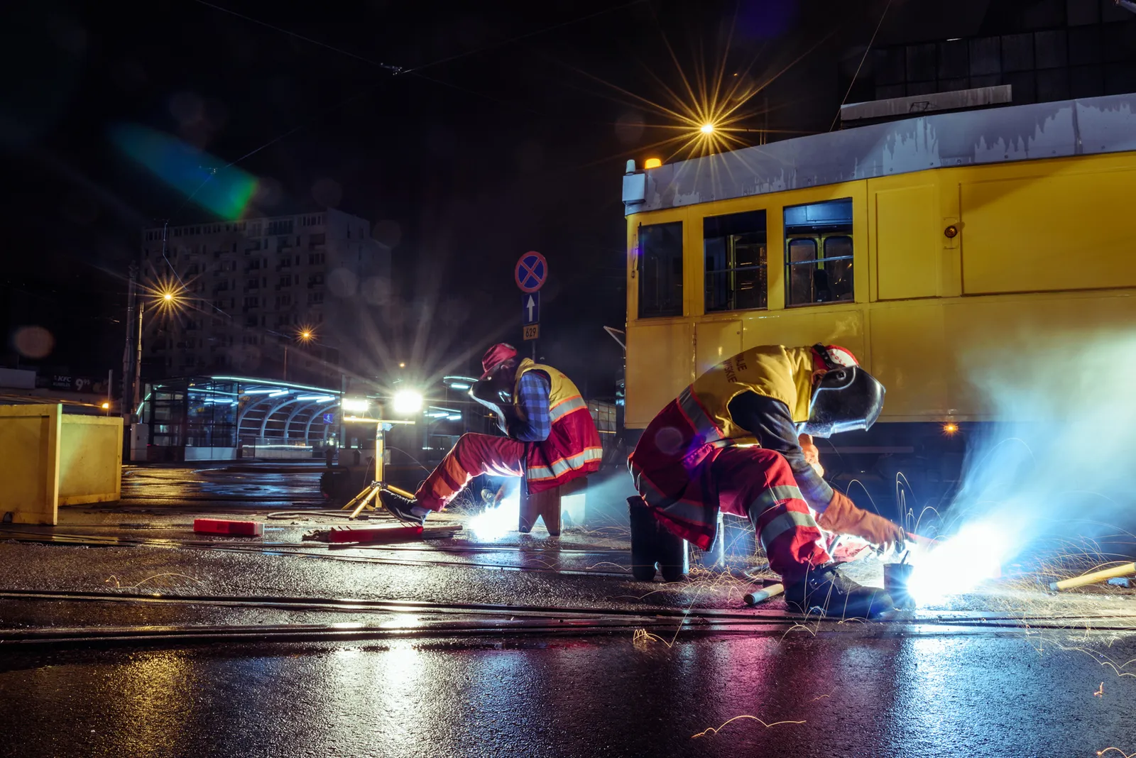 Workers welding beside a yellow tram at night
