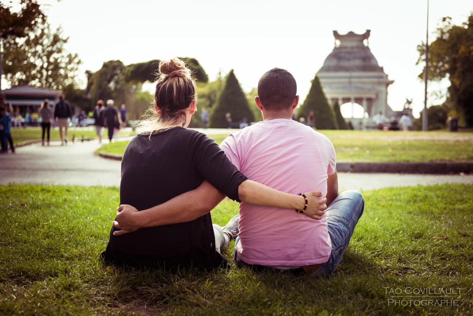 Couple sitting on grass with their backs to the camera and arms around each other.