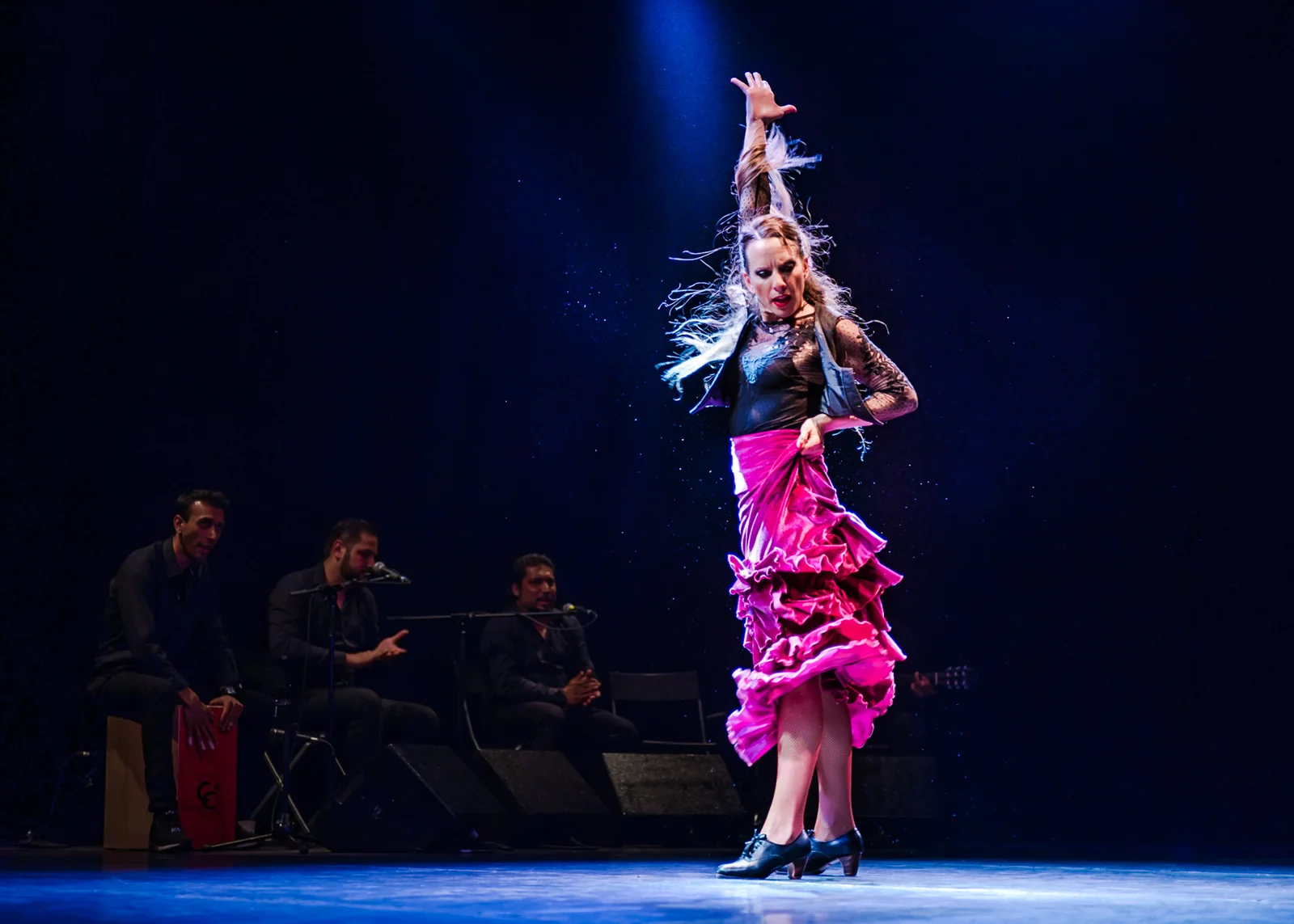 Flamenco dancer reaching upward under blue stage lighting.