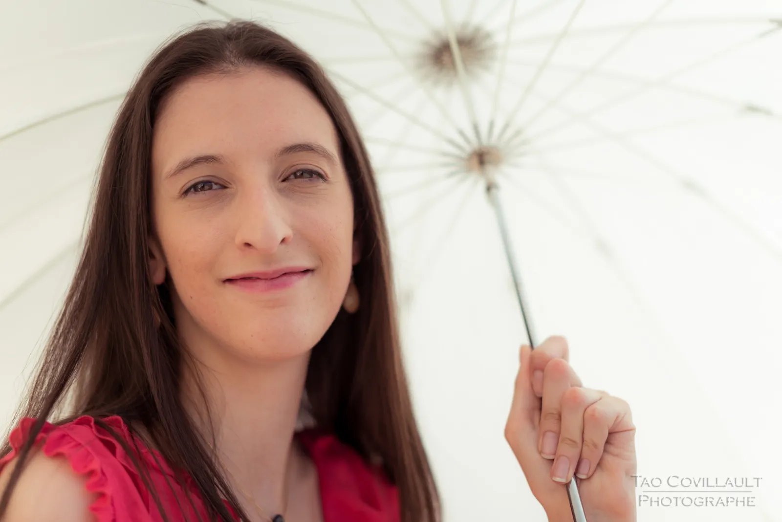 Woman in a bright pink top holding a white parasol.