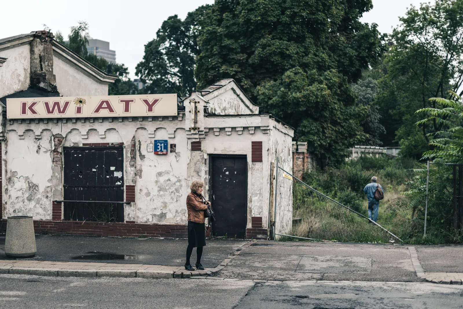 Person outside a weathered flower shop beside an overgrown lot