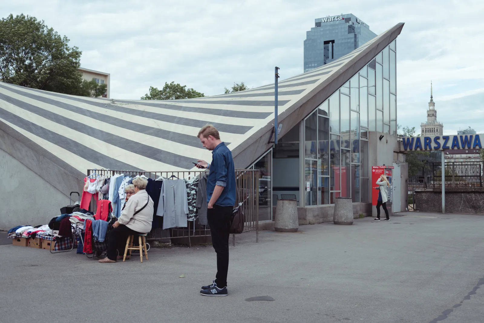 Person looking at a phone outside a Warszawa station entrance