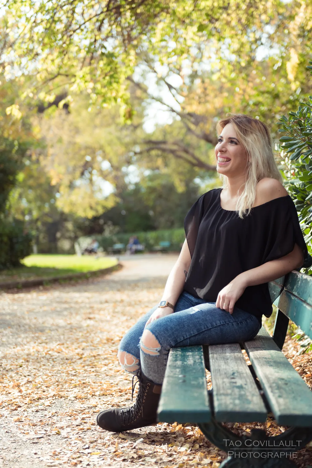 Woman in a black top and jeans seated on a green park bench.