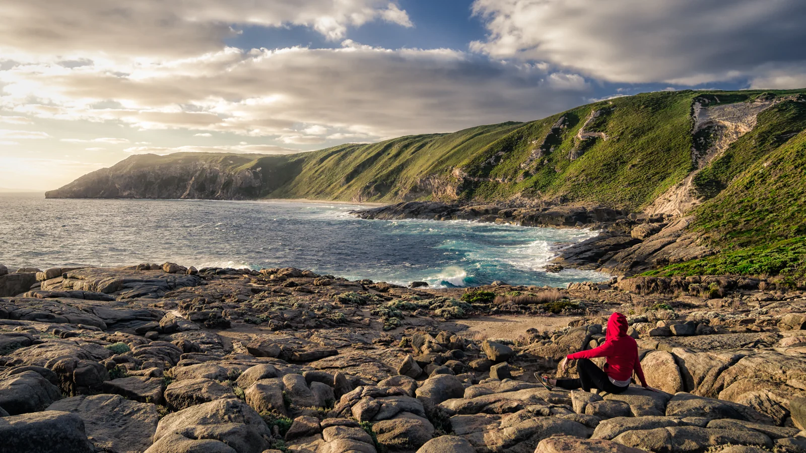 Person in a red jacket seated on a rocky coastline