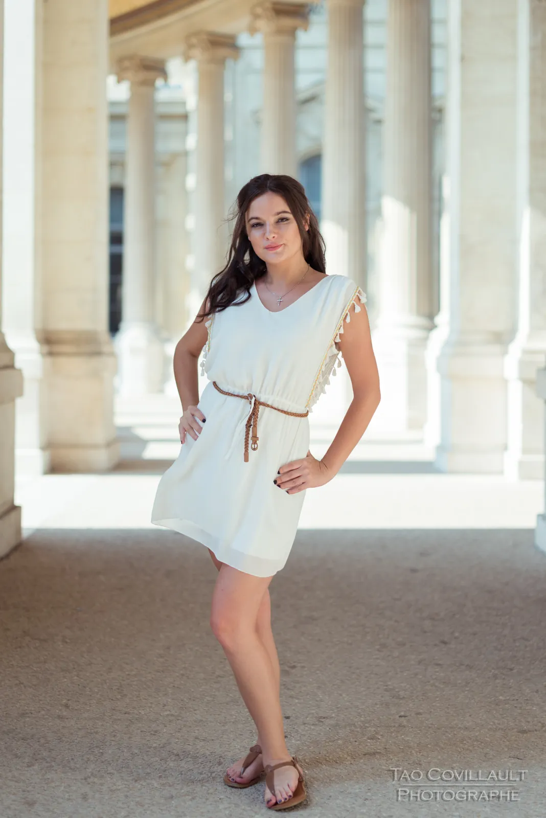 Woman in a white dress posing among pale stone columns.