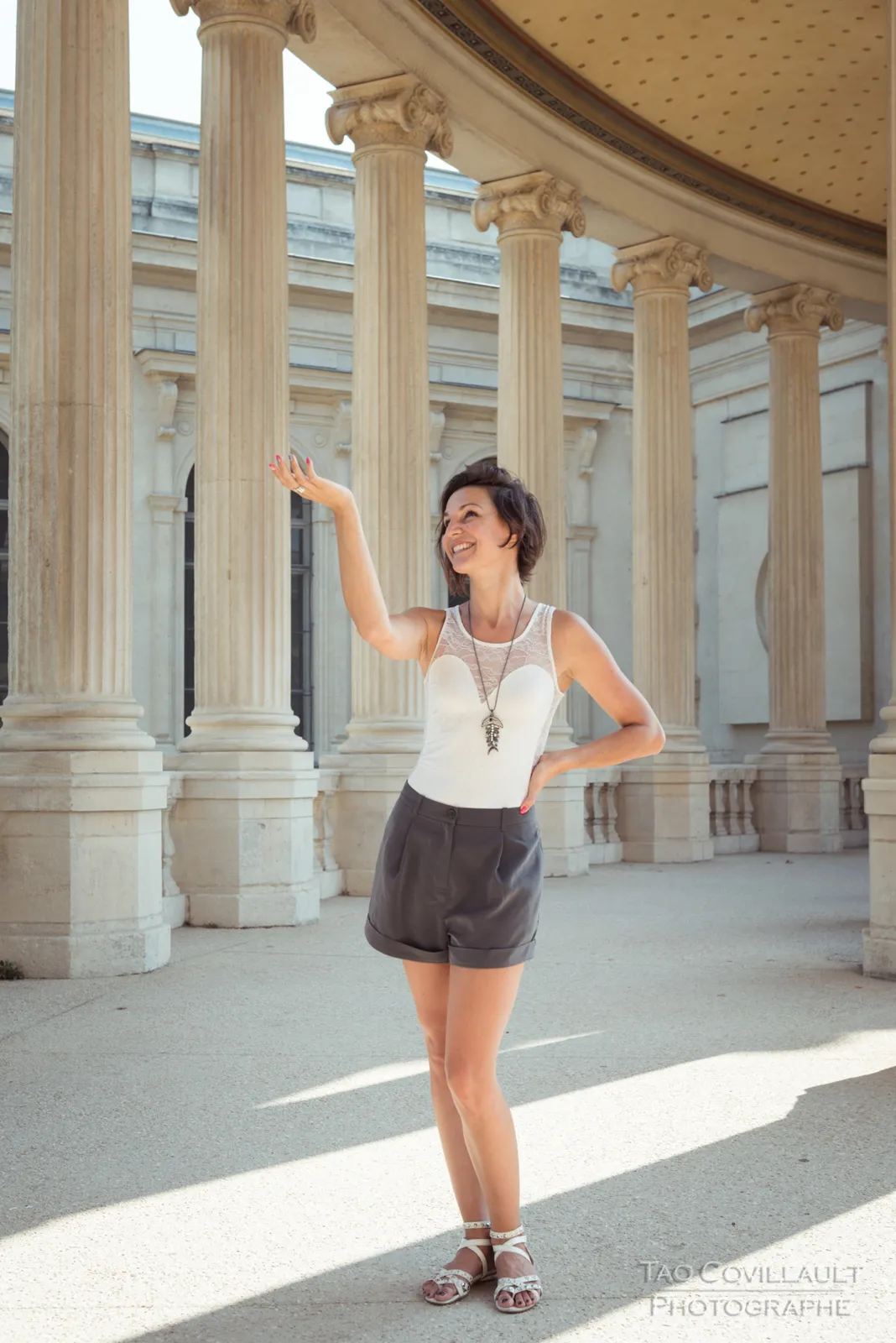 Woman in a white sleeveless top posing beside pale stone columns.