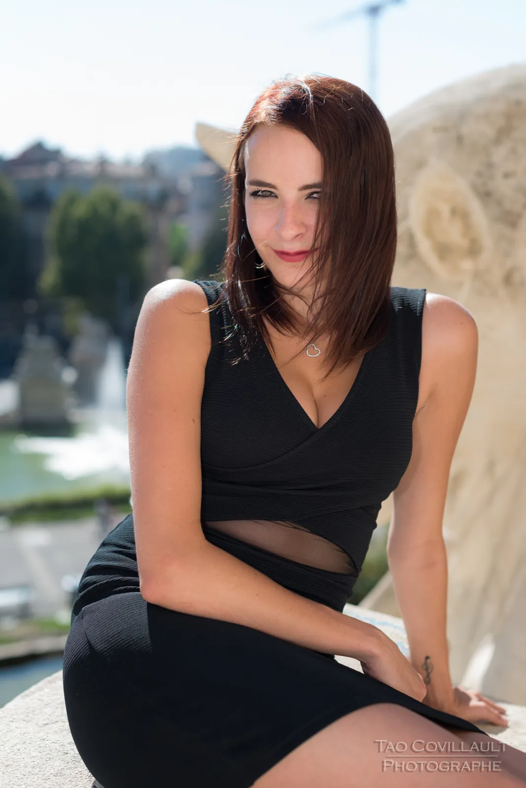 Woman in a black dress posing beside a stone balustrade.