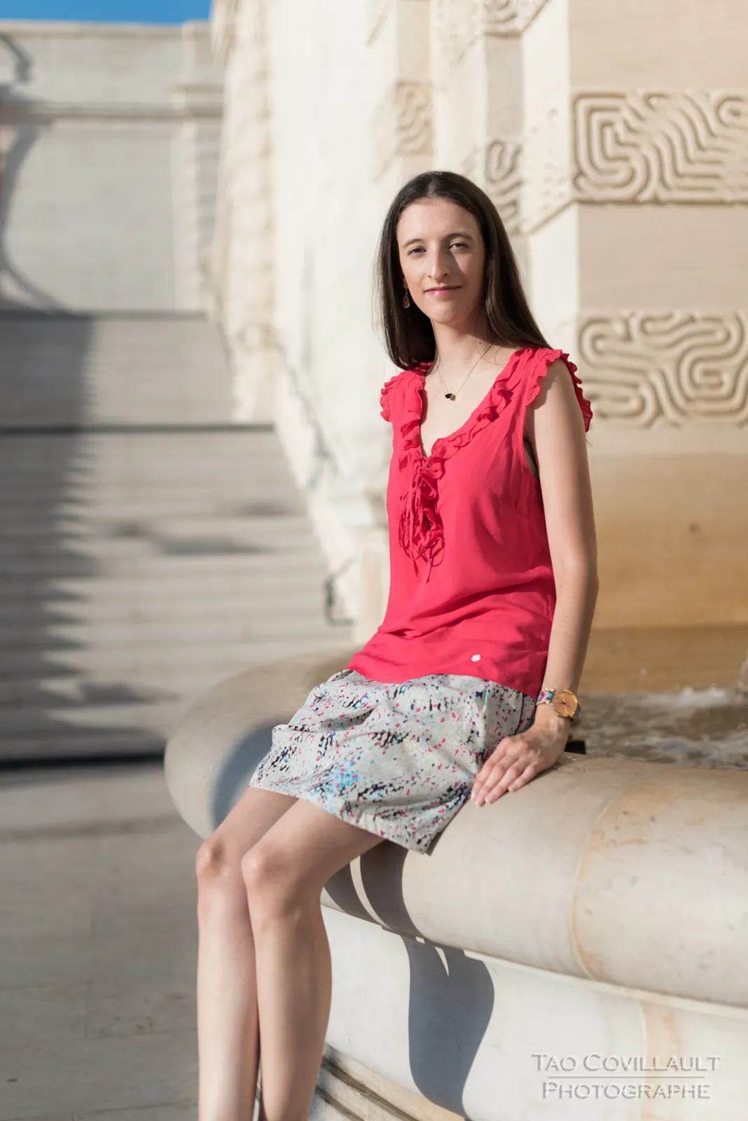 Woman in a bright pink top and patterned skirt posing beside stone steps and walls.