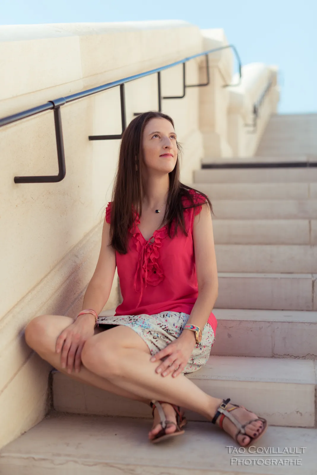 Woman in a bright pink top and patterned skirt posing beside stone steps and walls.
