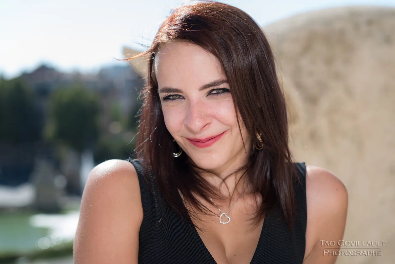 Woman in a black dress posing beside a stone balustrade.