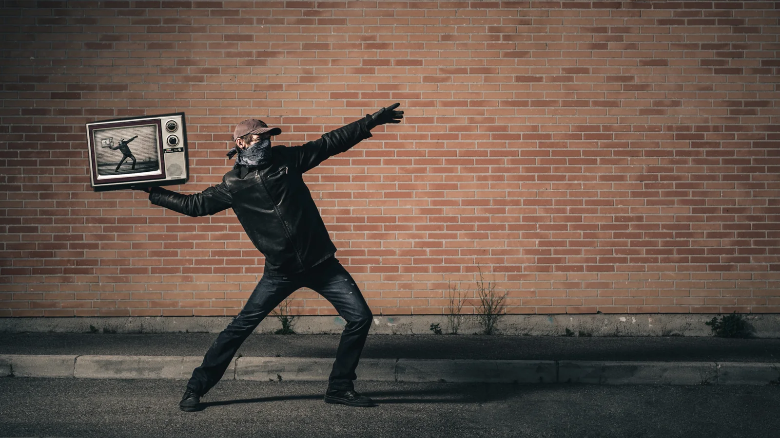 Person holding a picture frame in an outstretched pose by a brick wall