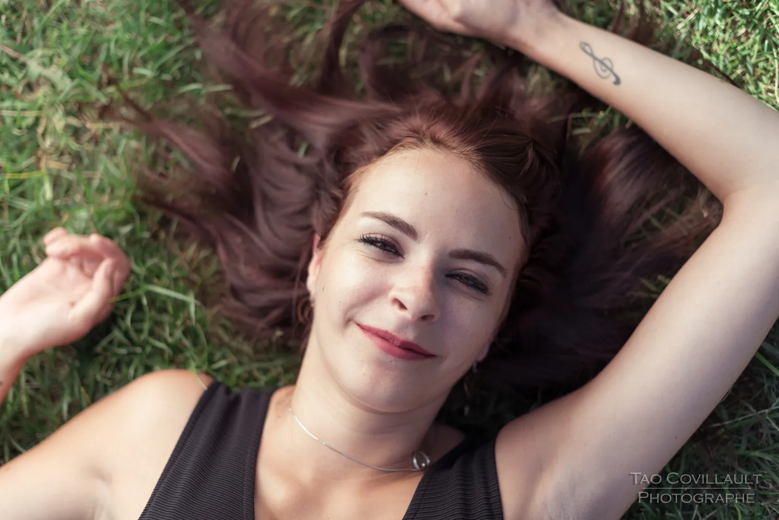 Woman lying on grass with her arms above her head.