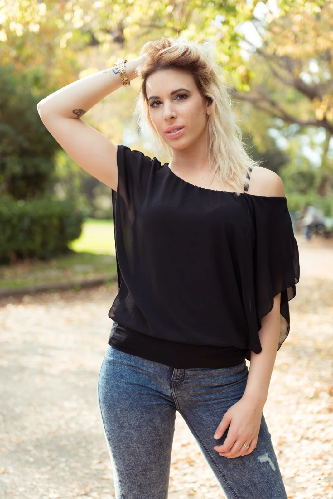 Woman in a black top and jeans posing in a leafy park.