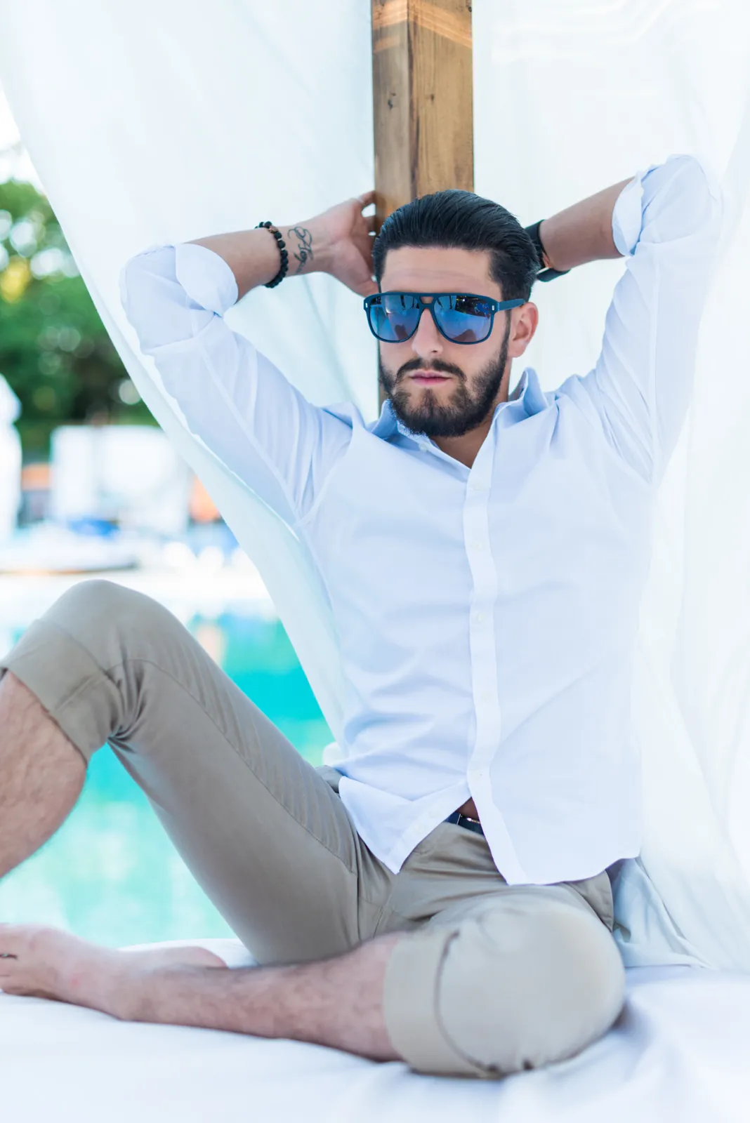 Man in a white shirt seated beneath poolside curtains.