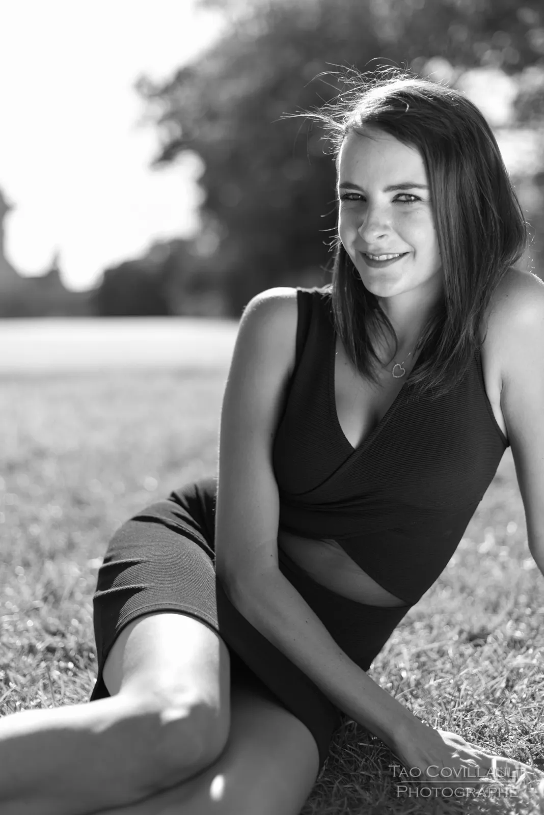 Black-and-white photograph: woman in a black dress relaxing on grass.