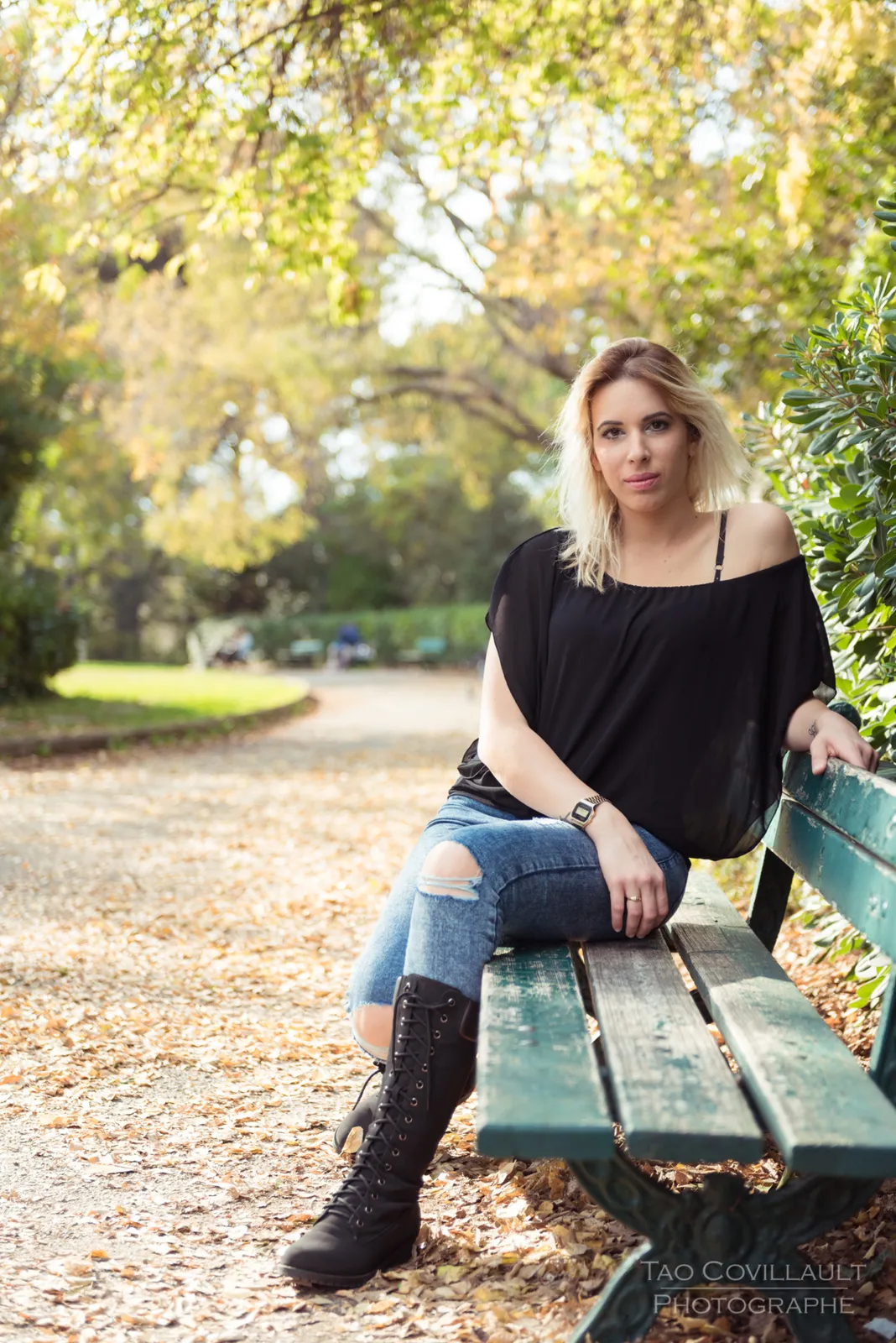 Woman in a black top and jeans seated on a green park bench.
