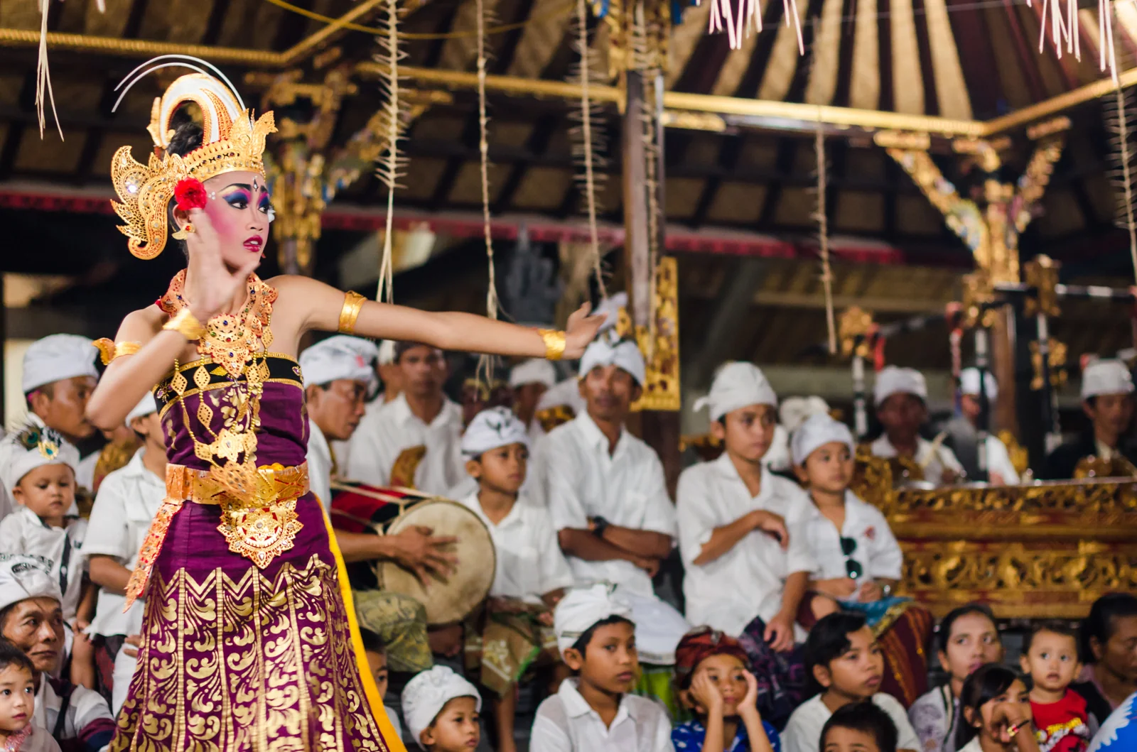 Dancer in an ornate golden headdress performing before an audience