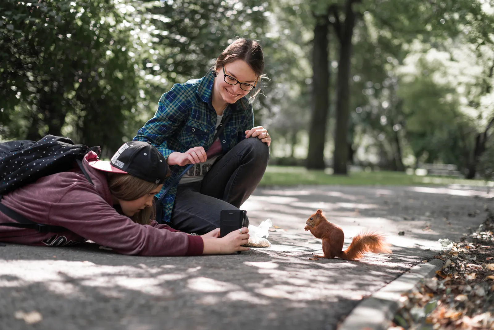 Two people photographing a squirrel on a park path