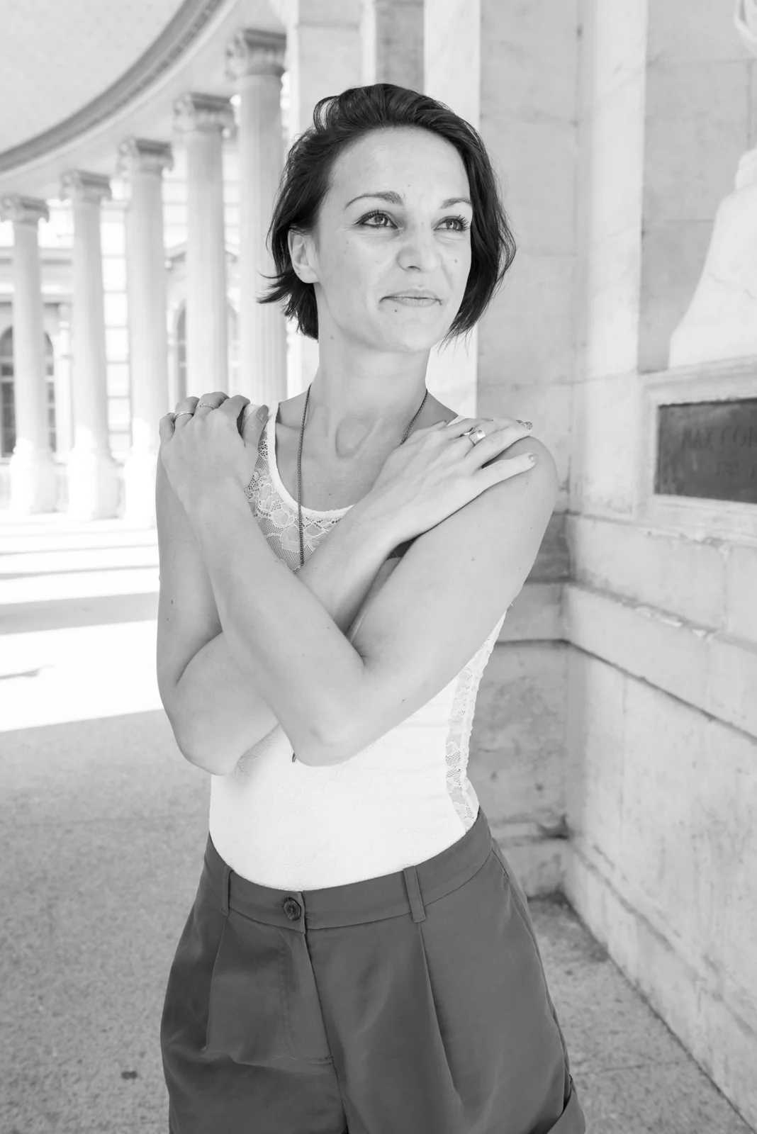 Black-and-white photograph: woman in a white sleeveless top posing beside pale stone columns.