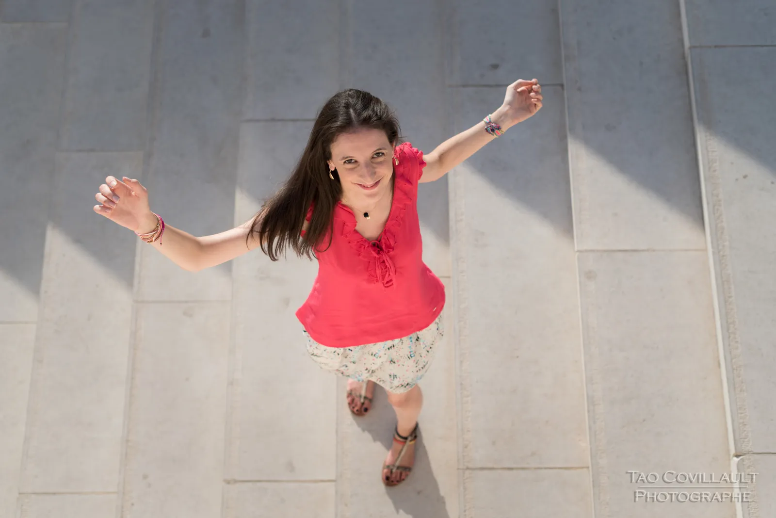 Woman in a bright pink top and patterned skirt posing beside stone steps and walls.