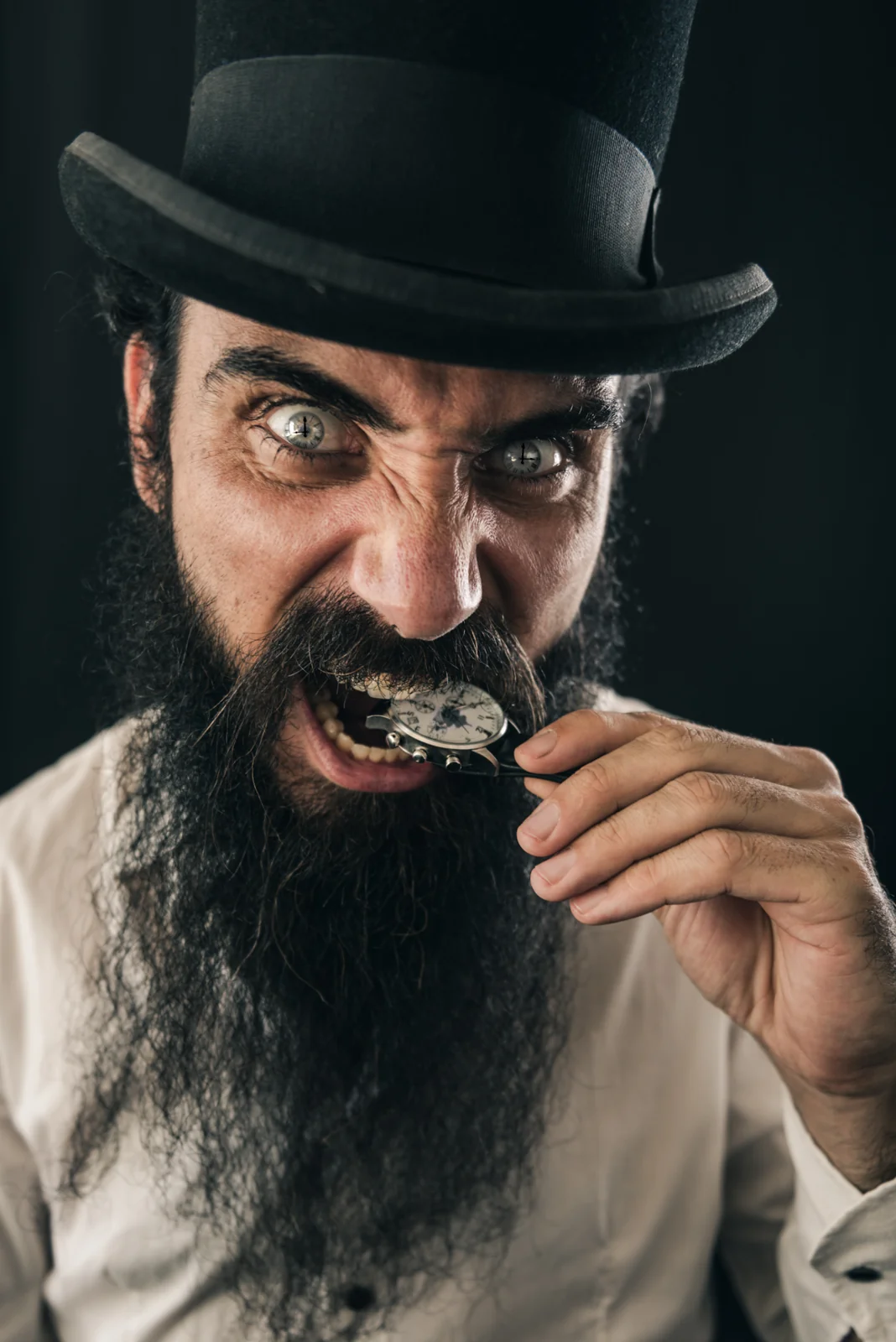 Bearded person in a top hat holding a small object near their mouth
