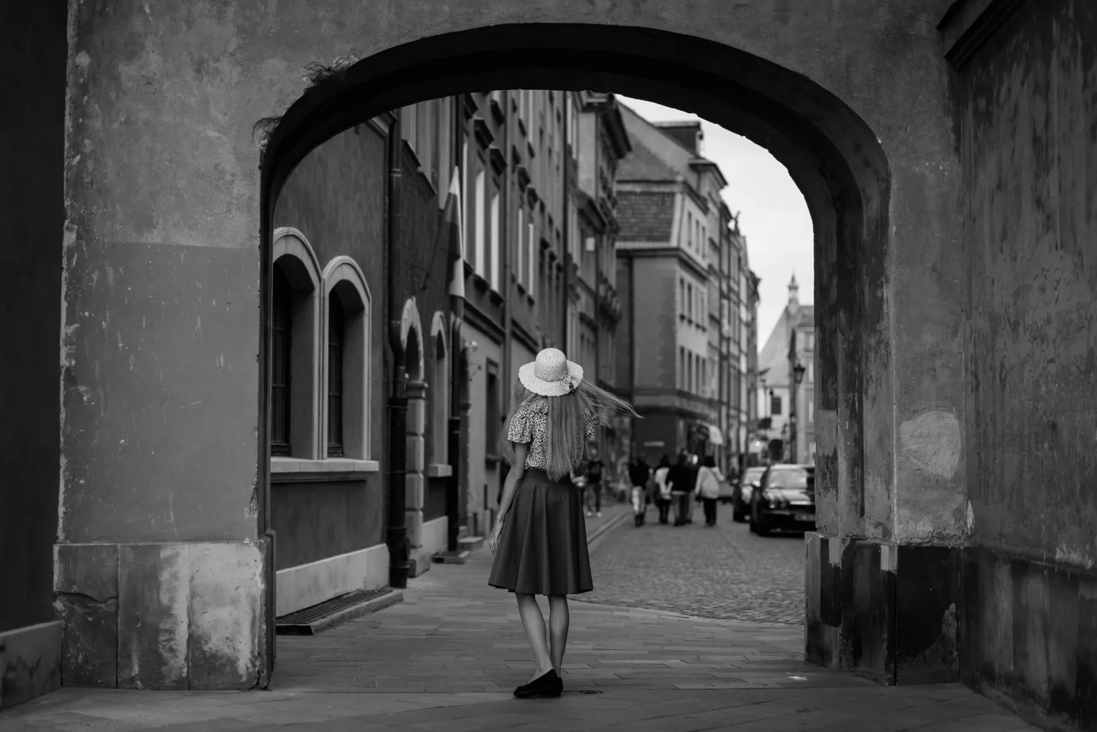 Person walking beneath an old stone archway in black and white