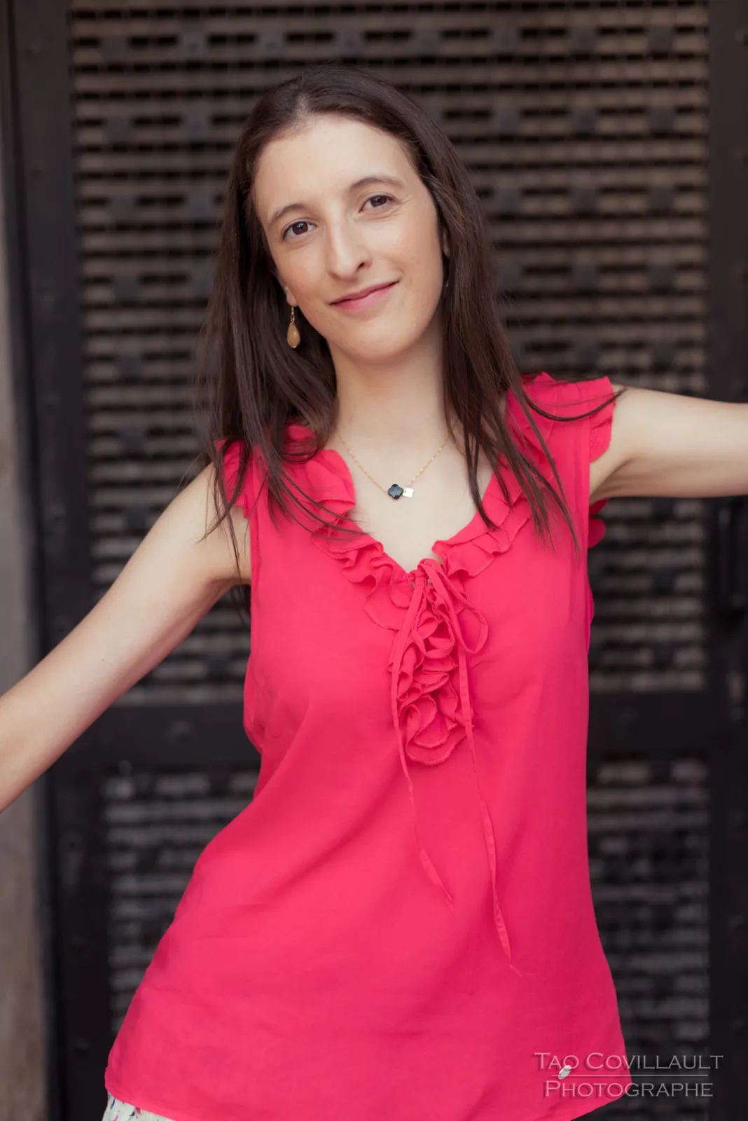 Woman in a bright pink top standing against dark shutters.